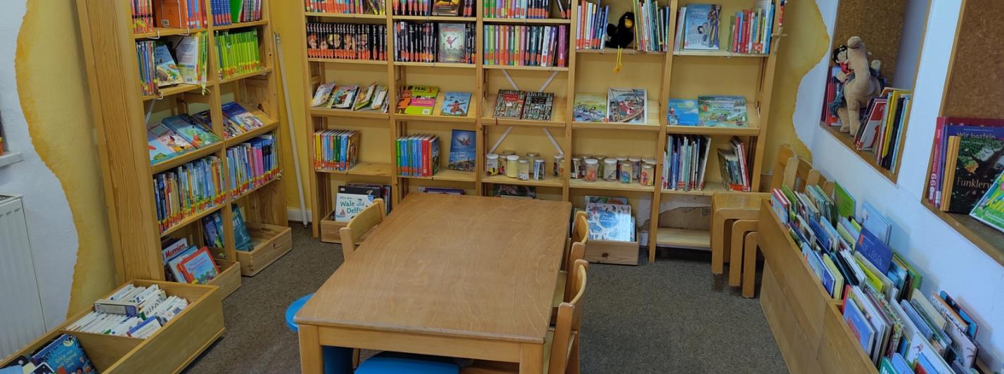 Kinderlesetisch mit Kinderbuchregalen im Hintergrund